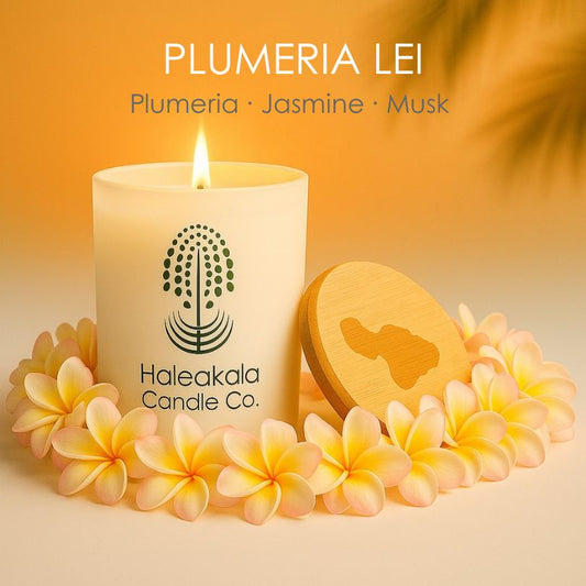 Haleakala Candle Co. candle with plumeria lei and wooden disc on a warm background